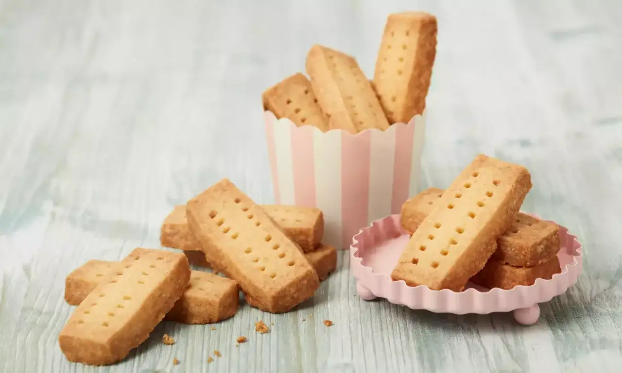 Goldbraune Shortbread-Riegel, perfekt f&uuml;r ein einfaches Shortbread Rezept, liegen auf einem rosa Teller und in einer gestreiften Schale.