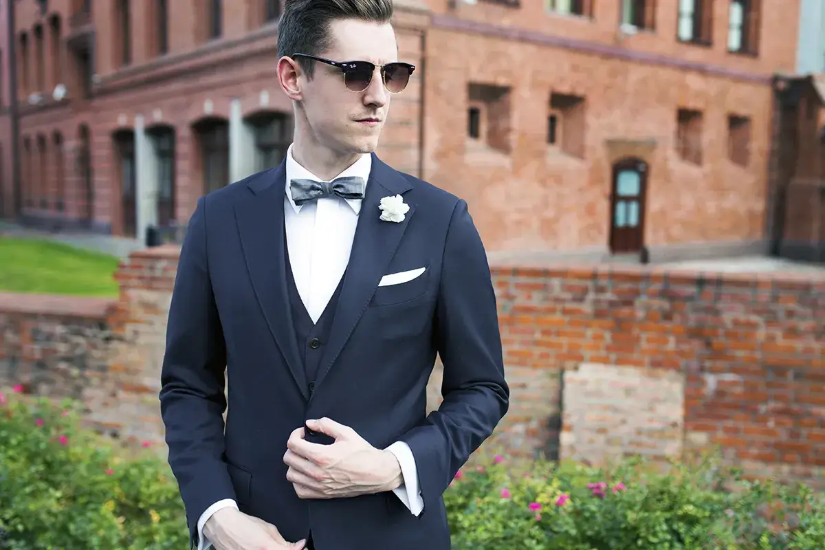 Elegancki mężczyzna w granatowym garniturze, białej koszuli i szarej muszce. Idealny wybór, jaki krawat do granatowego garnituru i białej koszuli na wesele.