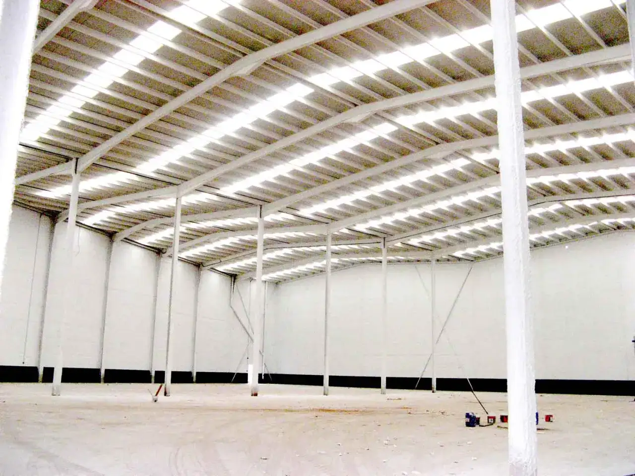 Interior de nave industrial en construcci&oacute;n, con estructura met&aacute;lica y techo transl&uacute;cido. Dise&ntilde;o de naves industriales funcional y moderno.