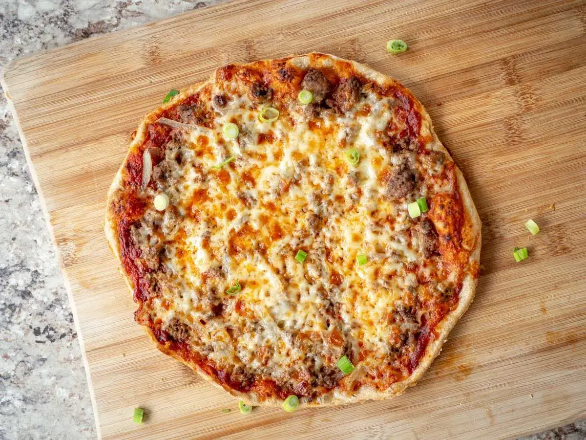 En saftig pizza med k&ouml;ttf&auml;rs och l&ouml;k, toppad med sm&auml;lt ost och garnerad med f&auml;rsk gr&auml;sl&ouml;k. Perfekt f&ouml;r en mysig kv&auml;ll.