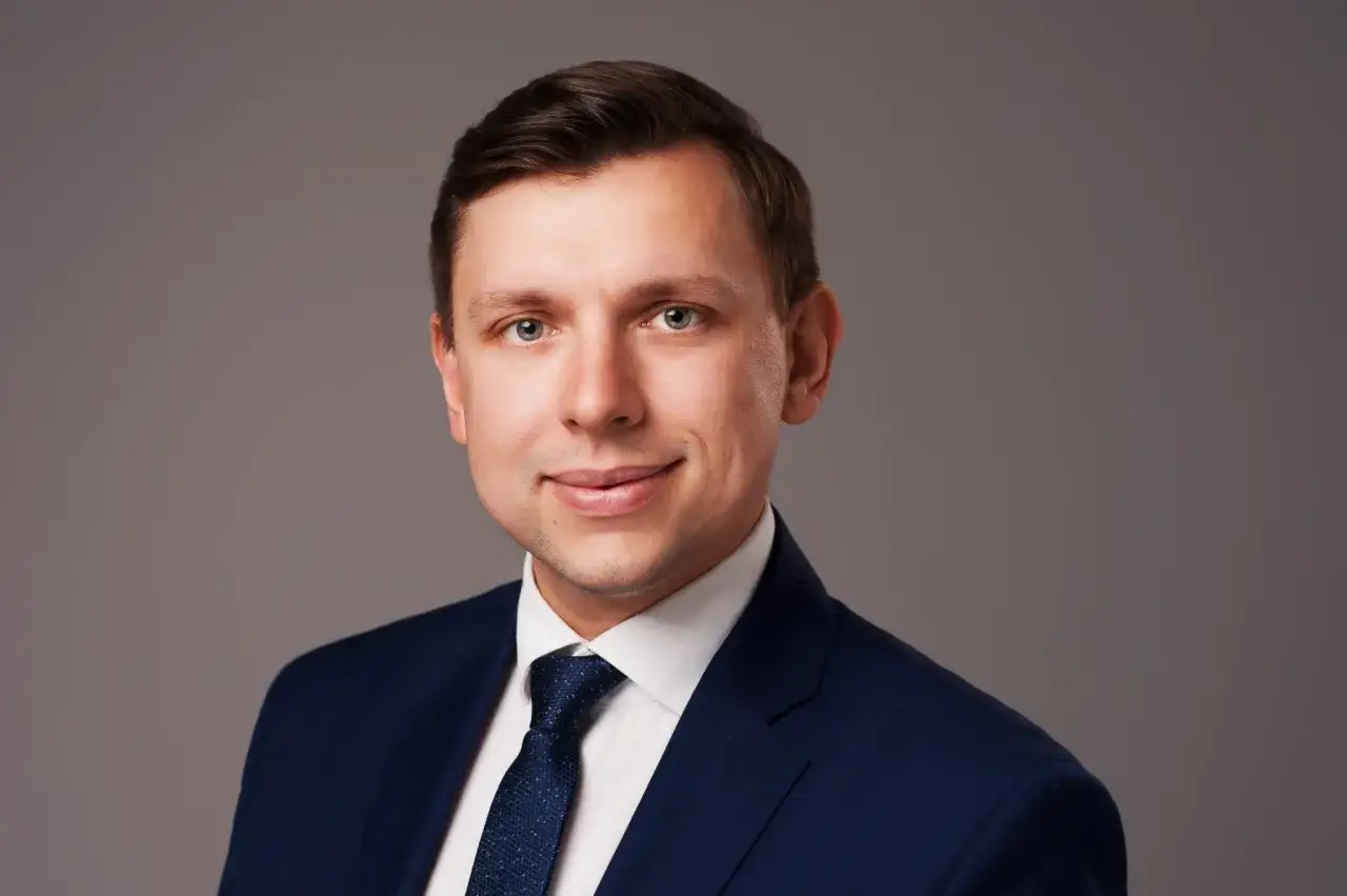 Portret mężczyzny w granatowym garniturze i białej koszuli z krawatem.