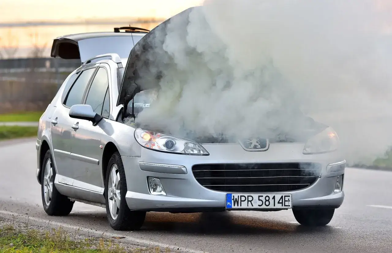 Srebrny Peugeot z otwartą maską i kłębami dymu. Silnik diesla ewidentnie ma problem, może to być rozbieganie silnika diesla.