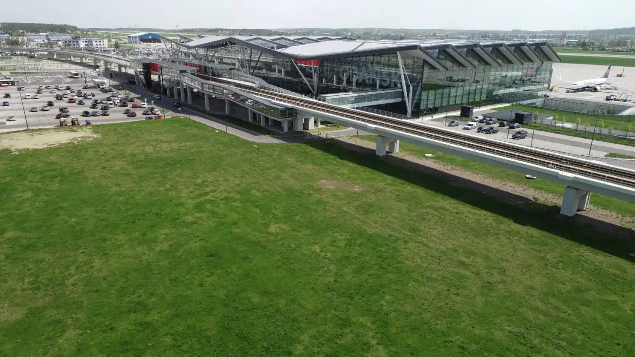 Nowoczesny terminal lotniska w Gdyni z kolejką naziemną i parkingiem pełnym samochodów.