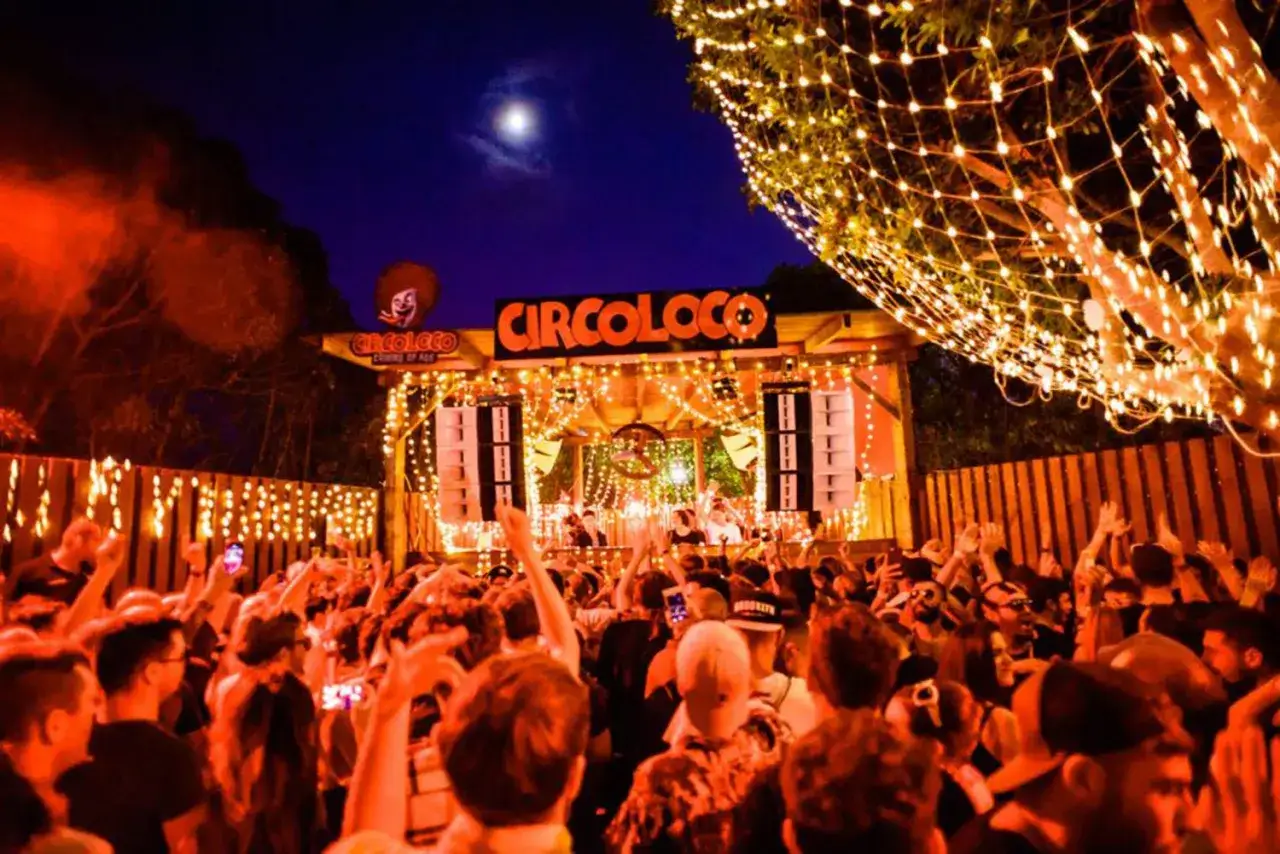 Folla in delirio a Circoloco, un evento notturno con luci, musica e un palco pieno di DJ.