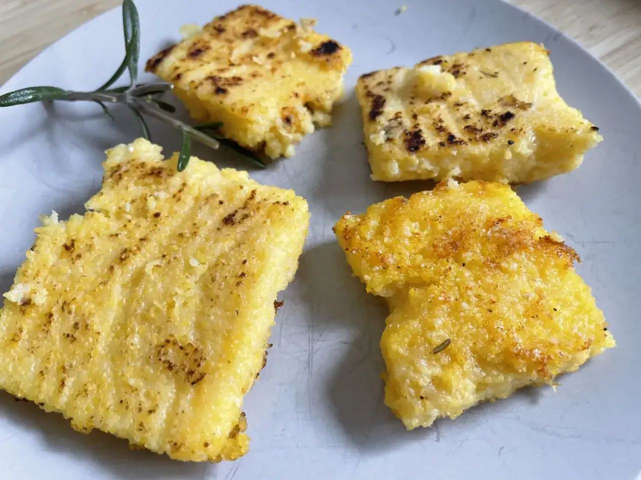 Gebratene Polenta-Quadrate auf einem Teller, garniert mit Rosmarin. Was ist Polenta? Ein herzhaftes Gericht aus Maisgrie&szlig;.