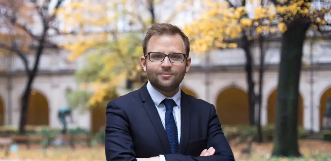 Un homme en costume bleu, lunettes, bras croisés, pose devant un bâtiment ancien. Il cherche des réponses : ma femme demande le divorce, quels sont mes droits ?