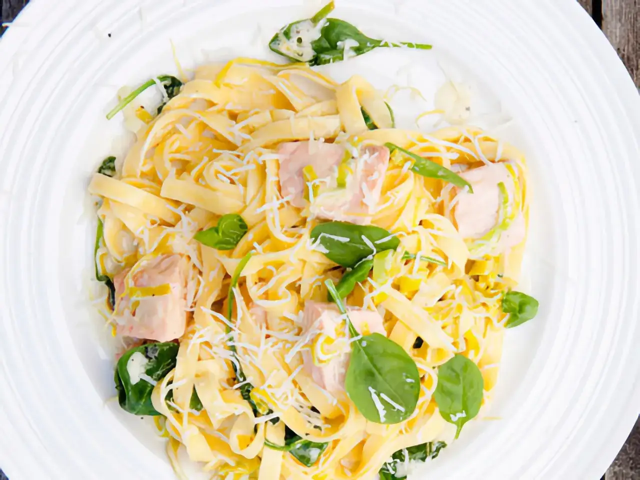 En kr&auml;mig laxpasta med f&auml;rsk spenat och riven parmesanost, serverad p&aring; en vit tallrik.
