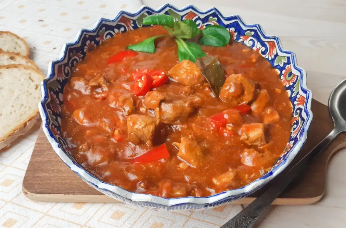 Aksamitny gulasz po węgiersku w ozdobnej misie, z kawałkami mięsa, papryki i chili. Obok kromki chleba. Idealny przepis na gulasz po węgiersku.