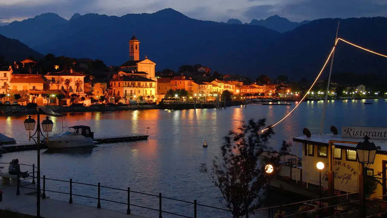 Serata sul Lago Maggiore: un borgo illuminato, montagne sullo sfondo e un ristorante galleggiante. Perfetto per scoprire cosa vedere in un giorno.