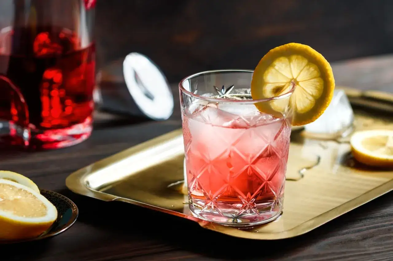 Ein erfrischender Americano Cocktail mit Eis und Zitronenscheibe auf einem goldenen Tablett.