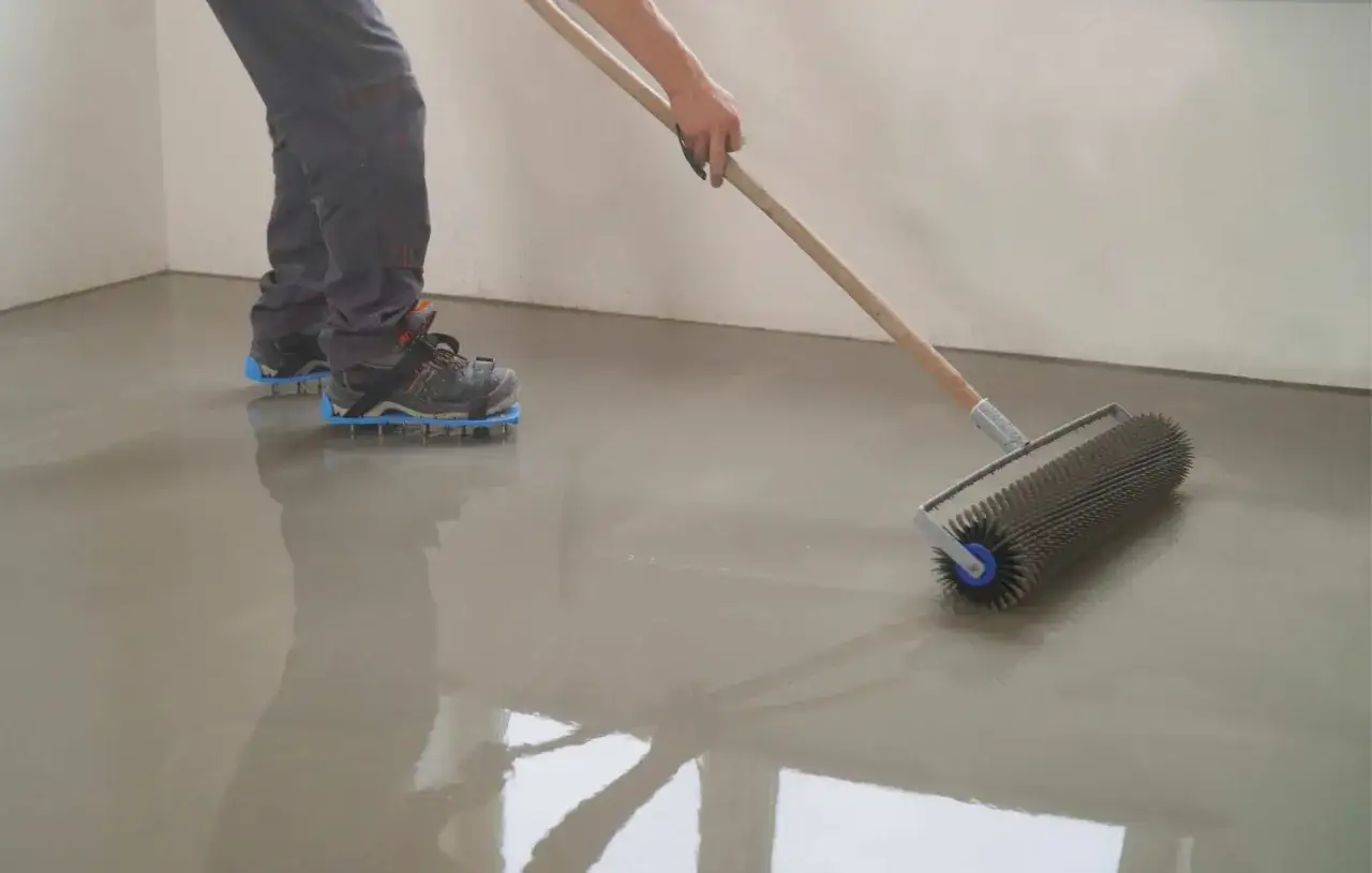 Persona con calzado de p&uacute;as usando un rodillo para nivelar un suelo reci&eacute;n vertido.