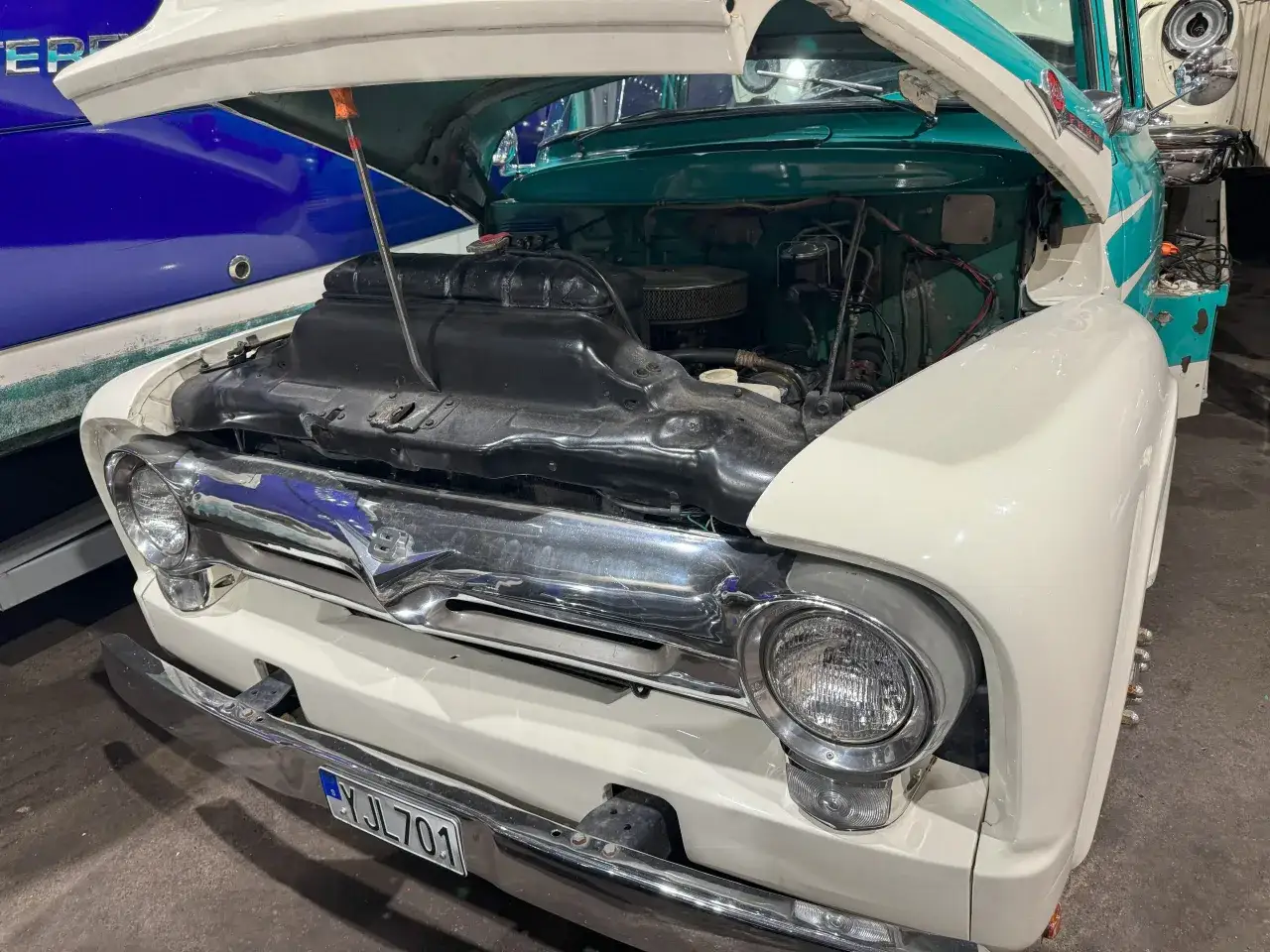 En vit och turkos Ford 56 med öppen motorhuv. En blå båt syns till vänster.
