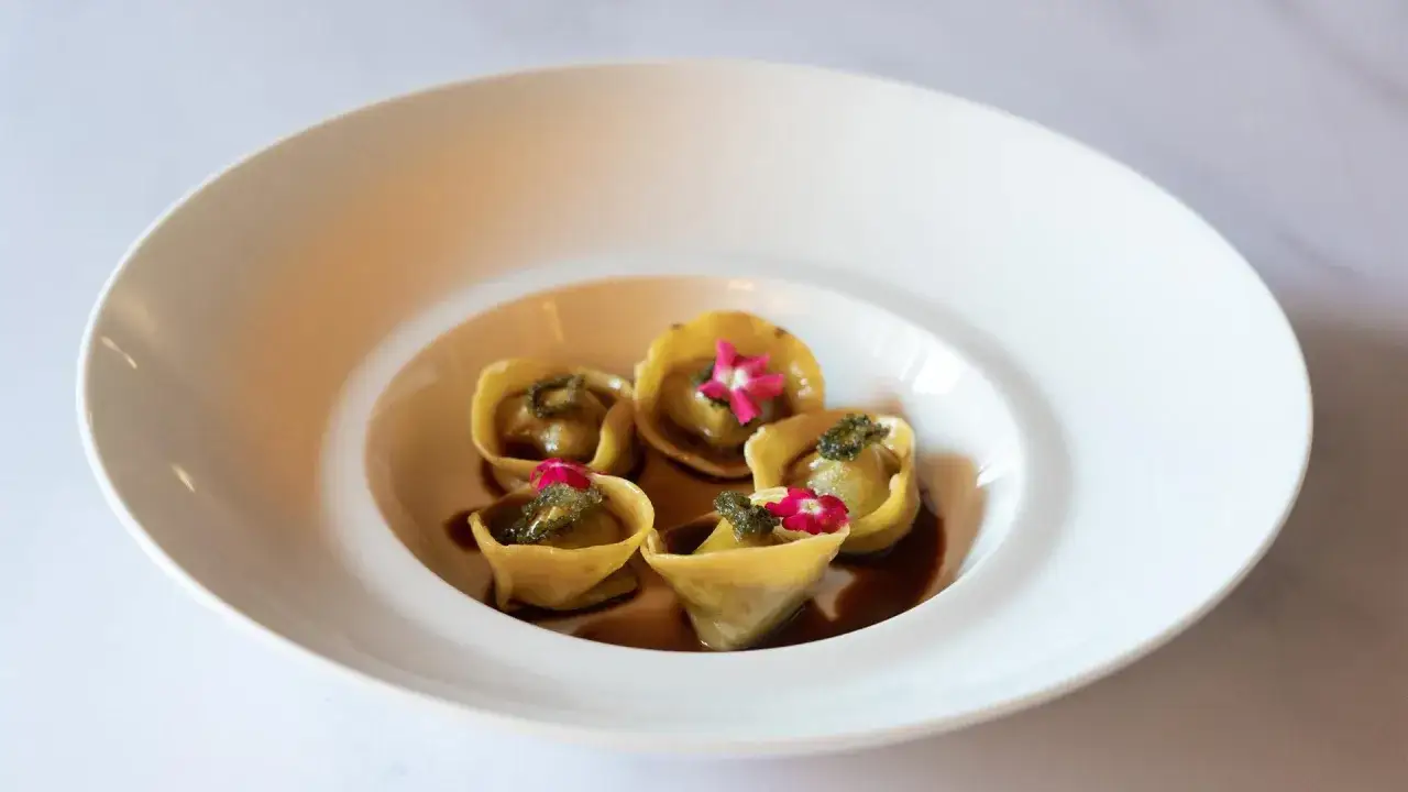 Ravioli dorati con ripieno verde e fiori rosa, un piatto che promette nuove stelle Michelin.
