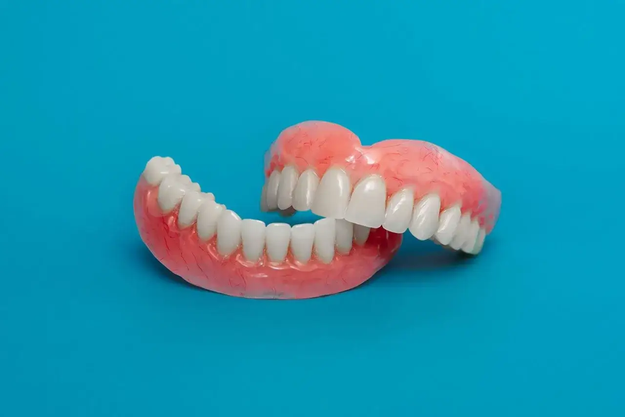 Un paio di dentiera mobile su sfondo blu, con denti bianchi e gengive rosa realistiche.