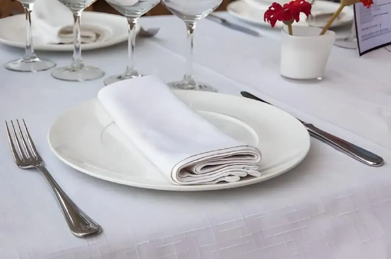Une assiette blanche avec une serviette de table pli&eacute;e, une fourchette et un couteau. La dimension serviette de table est parfaite pour cette pr&eacute;sentation &eacute;l&eacute;gante.
