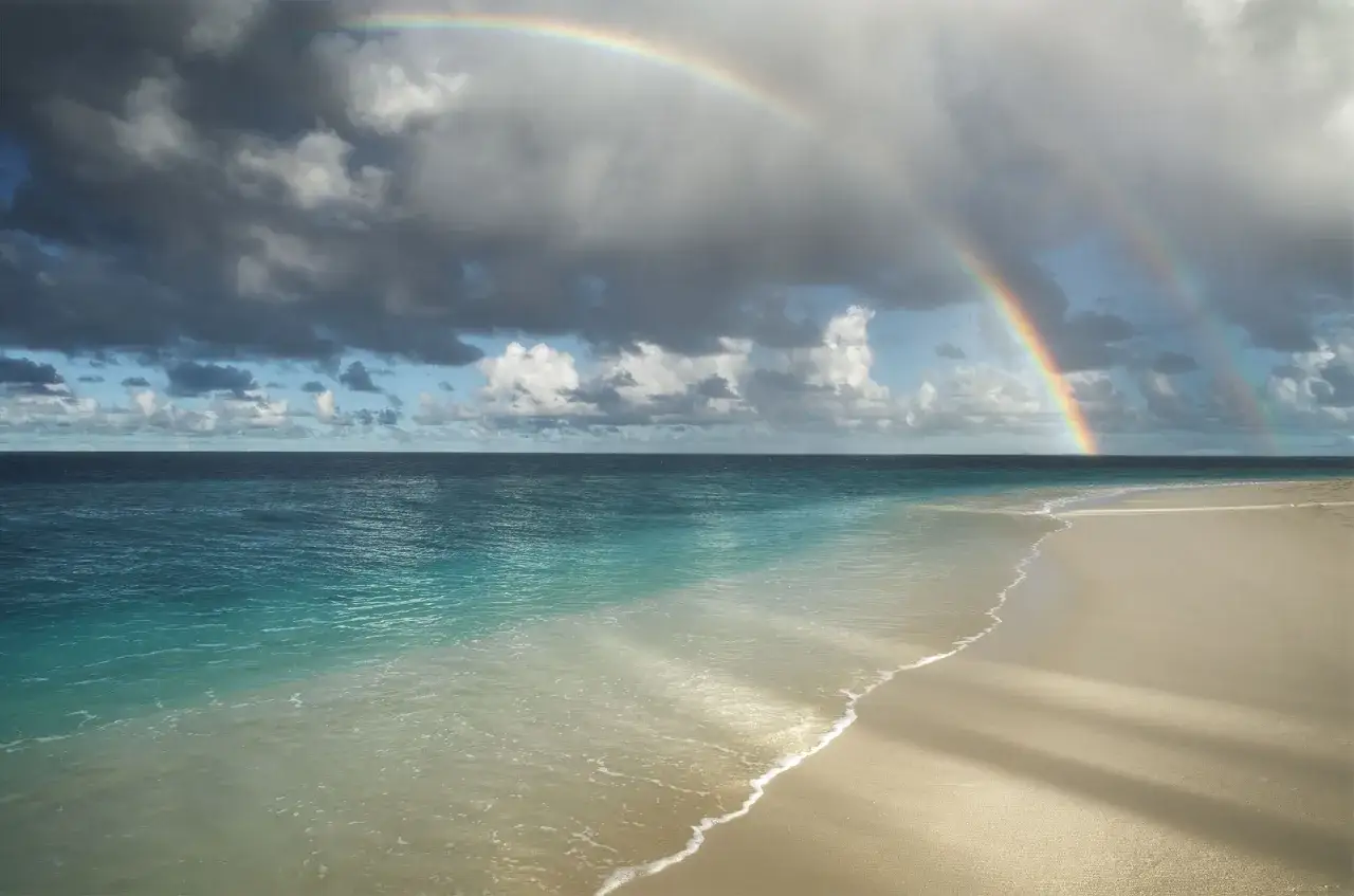 Ein doppelter Regenbogen über dem türkisfarbenen Meer und dem Sandstrand. Ein magischer Anblick im **Malediven November**.