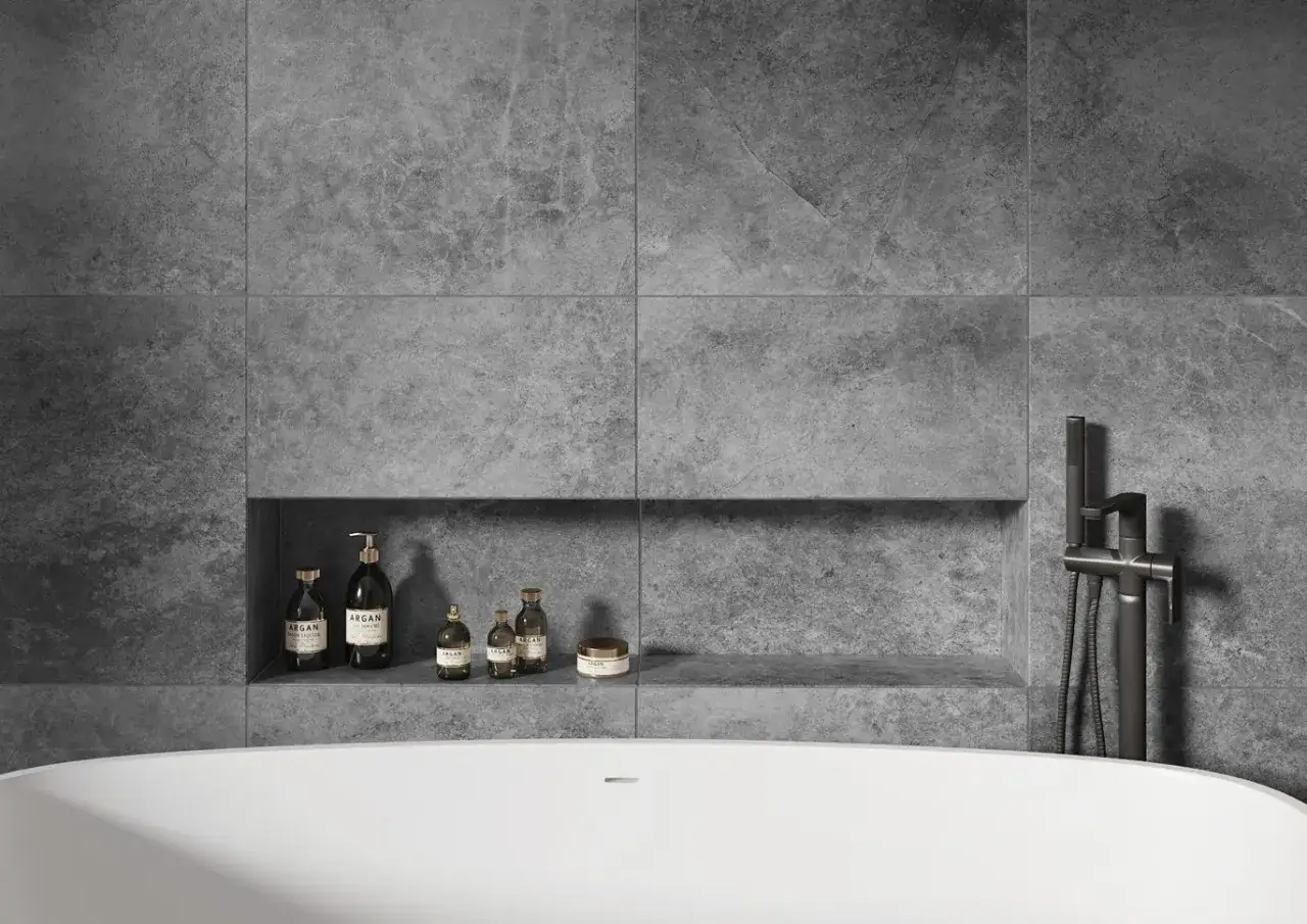 Nowoczesna półka nad wanną inspiracje: kosmetyki Argan i elegancka armatura łazienkowa na tle szarej, kamiennej ściany.
