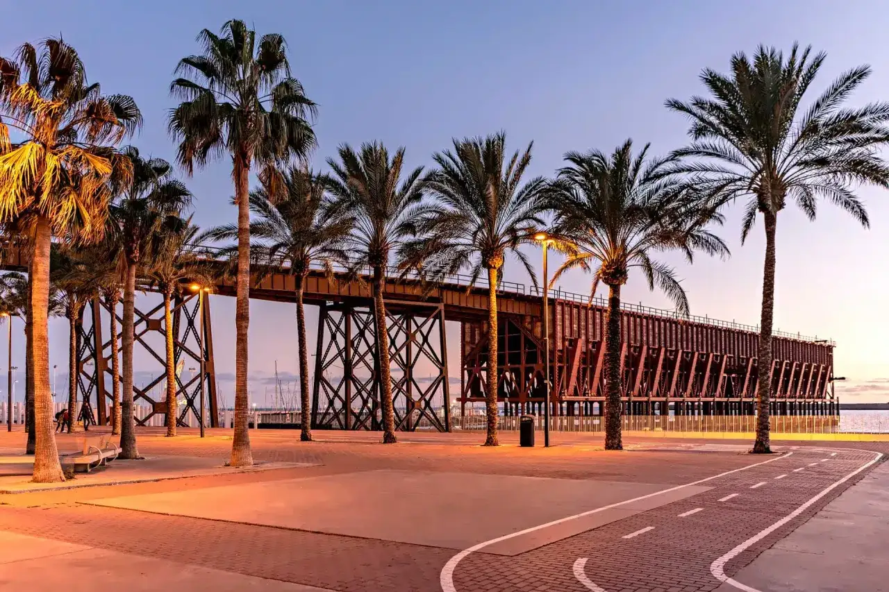 Palmeras y un muelle industrial al atardecer, ideal para el turismo Almería ciudad.