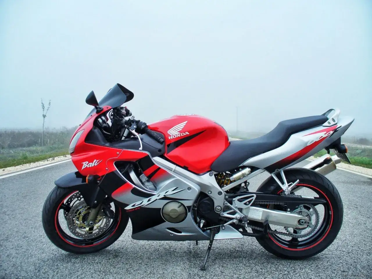 Czerwony motocykl Honda CBR600F z szarymi i czarnymi akcentami stoi na drodze w mglisty dzień.