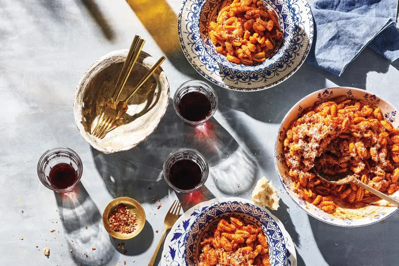 Assiette de malloreddus alla campidanese, pâtes traditionnelles sardes, servie avec du vin rouge et des flocons de piment.