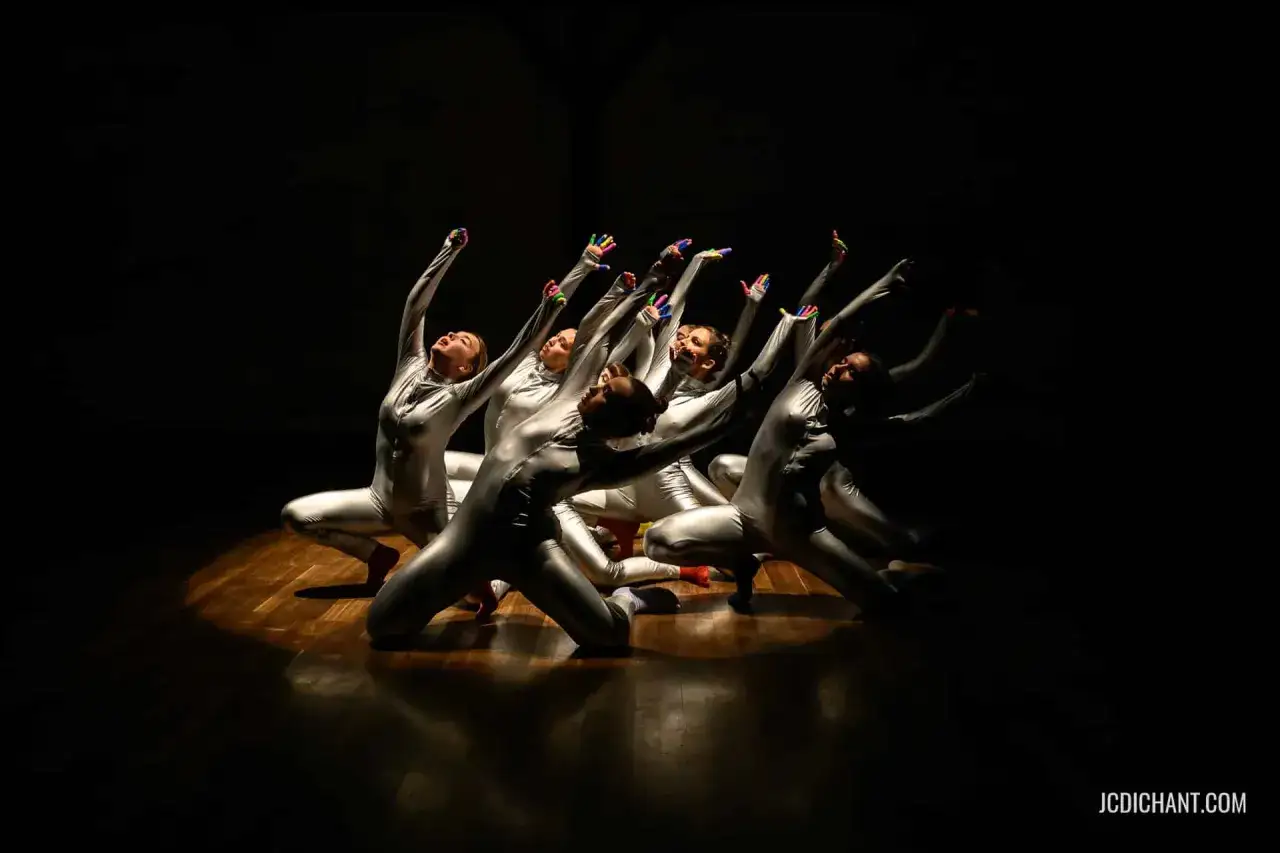 Un groupe de danseurs en costumes argentés, mains levées, dans un **photo spectacle** captivant.