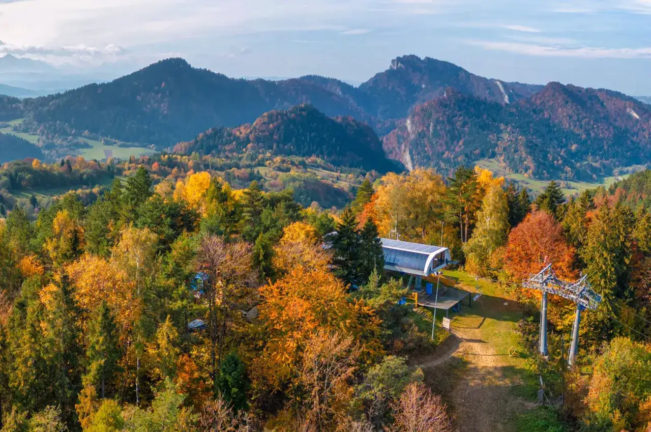 Jesienna panorama Pienińskiego Parku Narodowego z kolejką górską. Góry w tle, lasy w odcieniach złota i czerwieni.