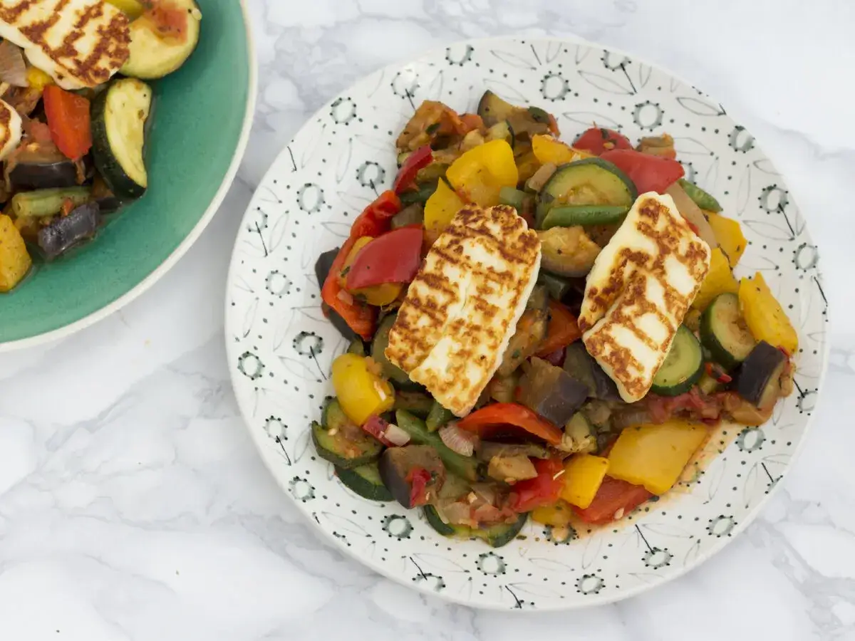 Dwa talerze z ratatouille i grillowanym serem halloumi. Warzywa są kolorowe, a ser ma charakterystyczne paski.
