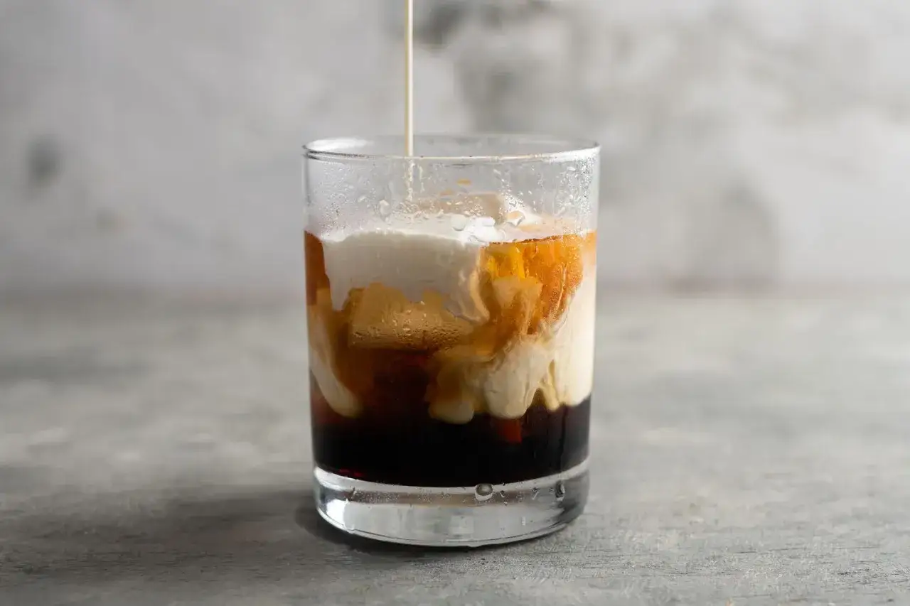 Gr&auml;dde virvlar ner i en m&ouml;rk v&auml;tska i ett glas, vilket skapar ett vackert m&ouml;nster som p&aring;minner om en White Russian.