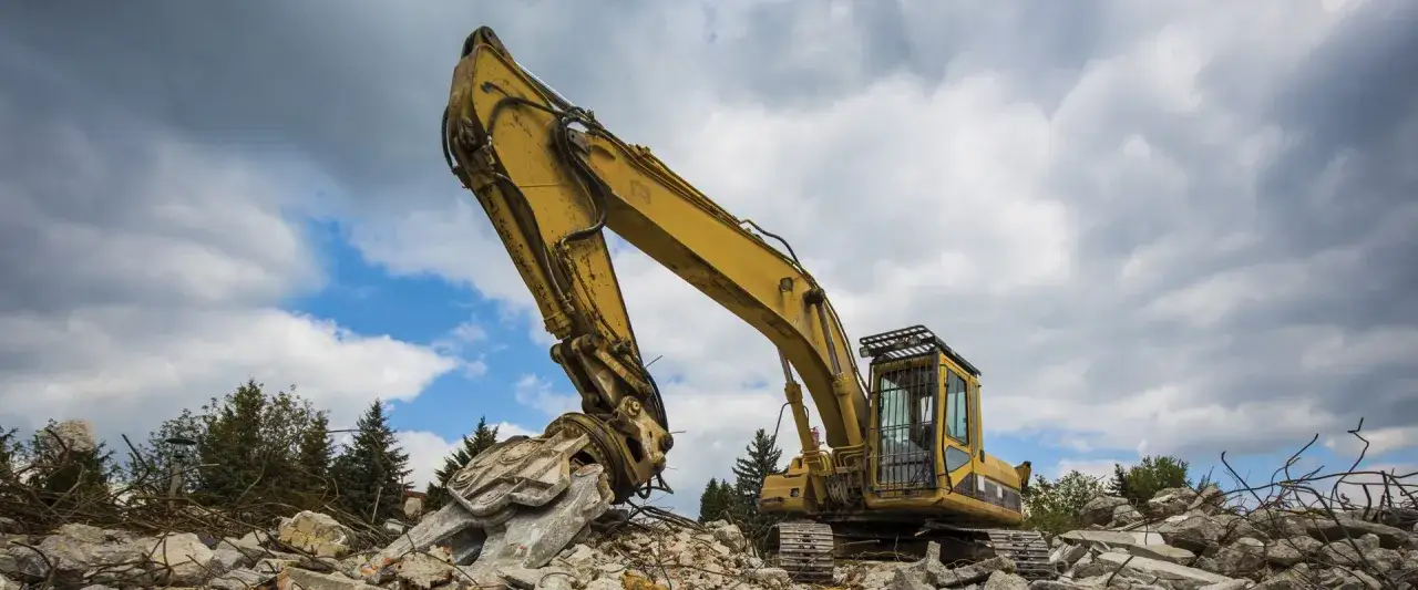Escavatore giallo su cumuli di macerie, simbolo del **materiale di risulta** e della demolizione.