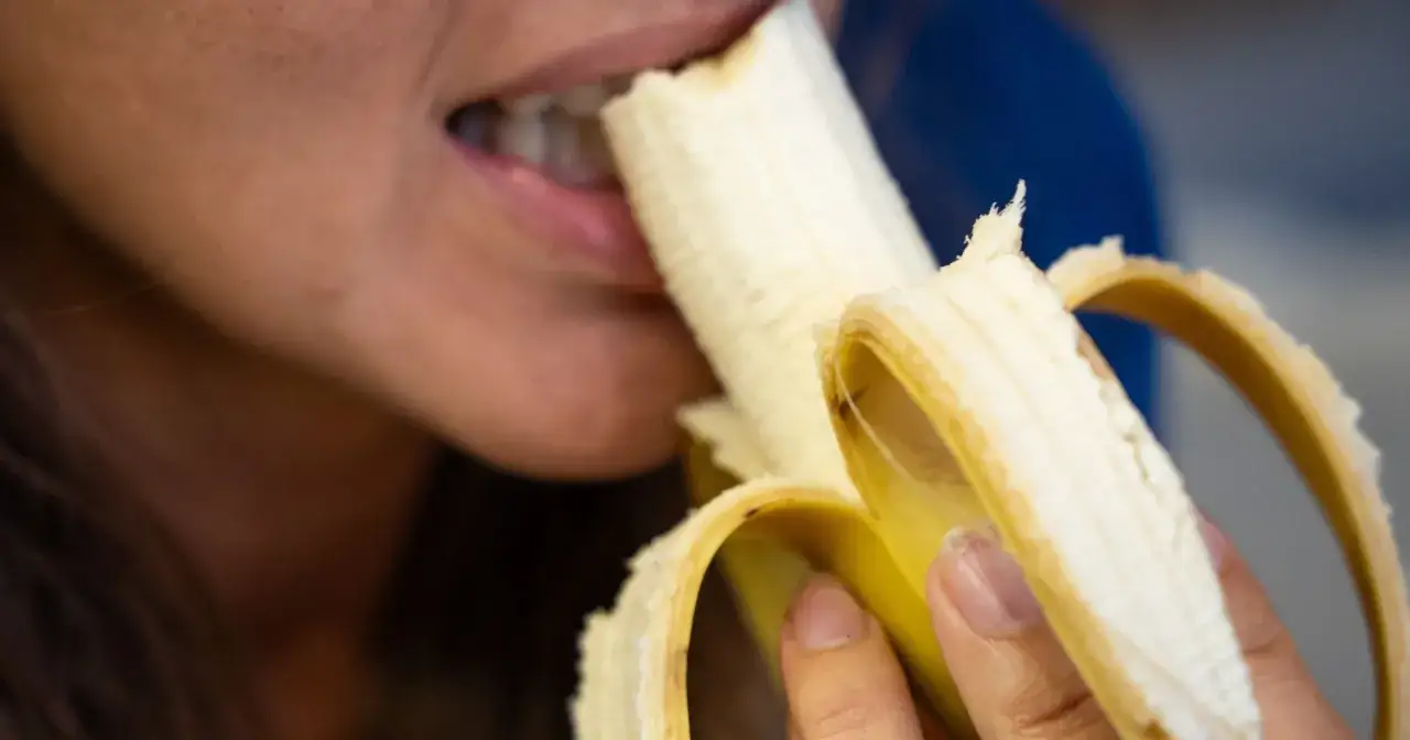 Kobieta gryzie banana, idealny posiłek na pusty żołądek.