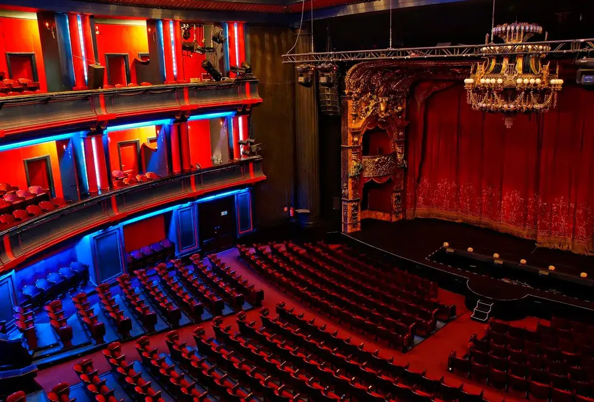 Wnętrze teatru Roma. Czerwone fotele i kurtyna, ozdobne balkony z neonowym oświetleniem. Czekamy na spektakl.