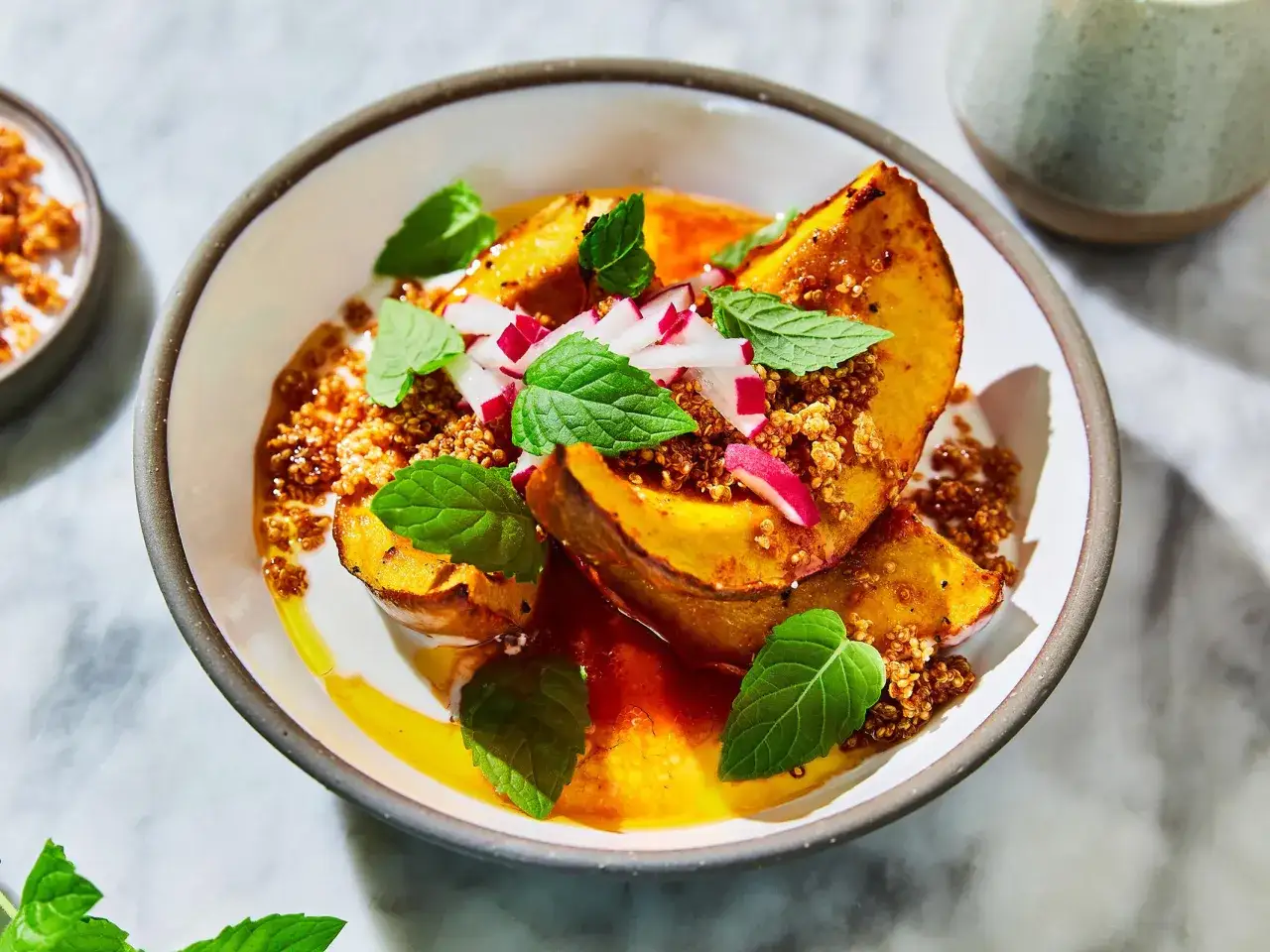 Tranches de courge butternut rôties, nappées d'une sauce dorée, garnies de quinoa croustillant, de radis et de feuilles de menthe fraîche.