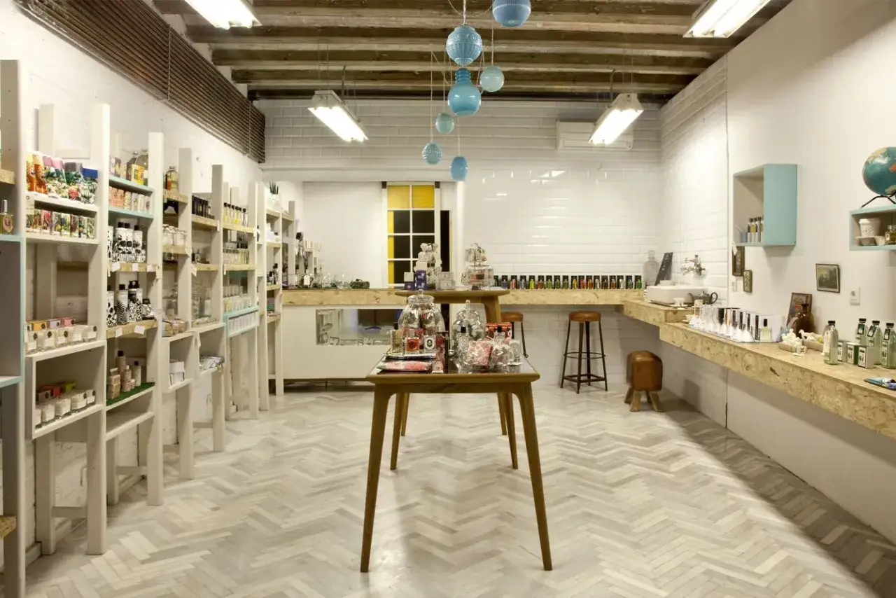 Tienda de cosméticos con estanterías llenas de productos, mesas de exhibición y un mostrador con botellas. El diseño minimalista evoca la tranquilidad de un laconicum.