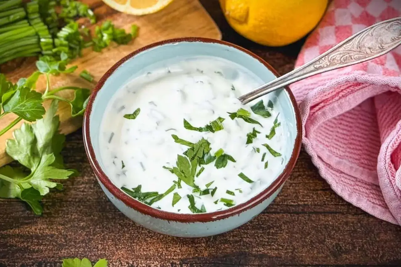 Cremiger Knoblauch Joghurt Dip mit frischer Petersilie, bereit zum Dippen. Daneben liegen Zitronenspalten und Kr&auml;uter.