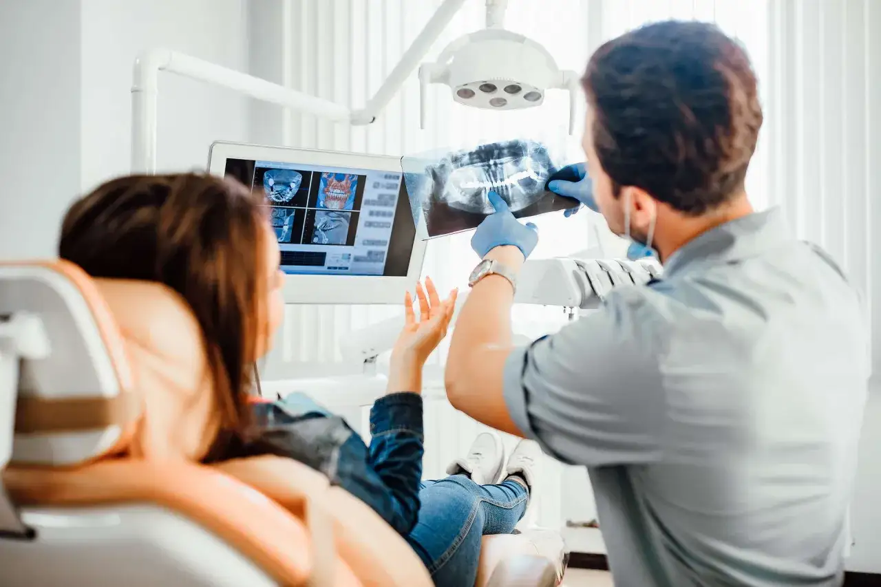Stomatolog omawia z pacjentką zdjęcie rentgenowskie zębów, wyjaśniając diagnozę.