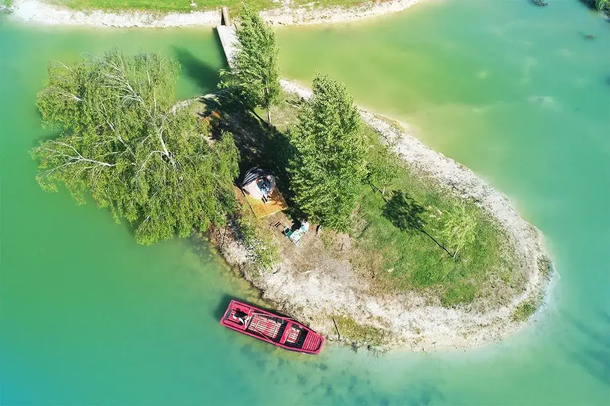 Un séjour insolite en Île-de-France : une petite île avec une cabane, un bateau rouge et un ponton.