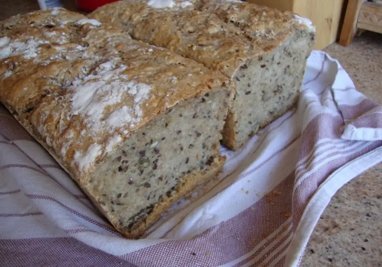 Dwa bochenki chleba na zakwasie, z widocznym ziarnem w środku, leżą na ręczniku. Idealny chleb na zakwasie przepis.