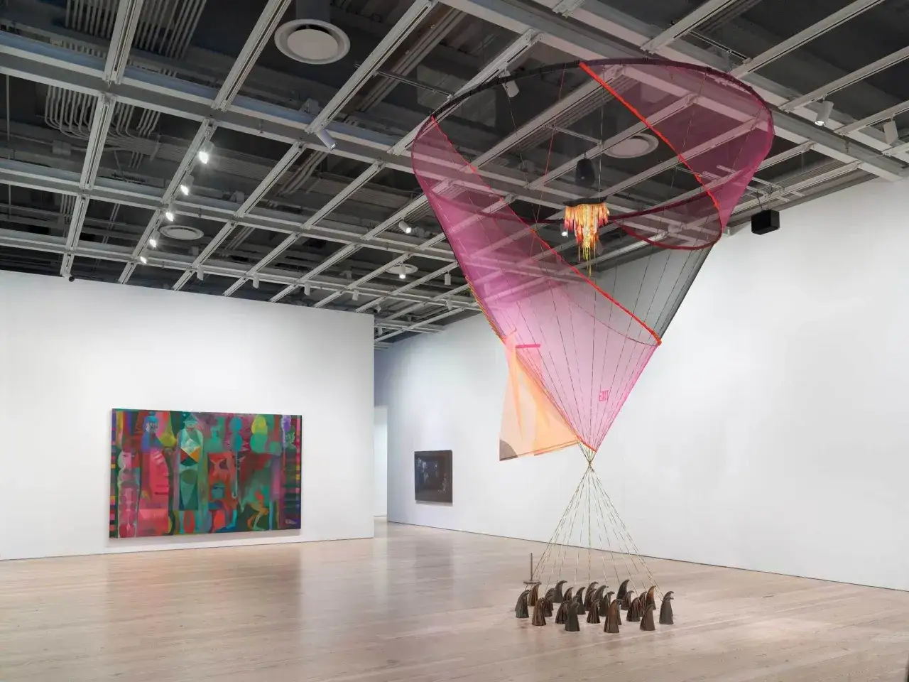 A vibrant installation at the Whitney Biennial 2026 features a large, pink and orange parachute-like sculpture suspended from the ceiling, with a cluster of bird-like figures on the floor below.