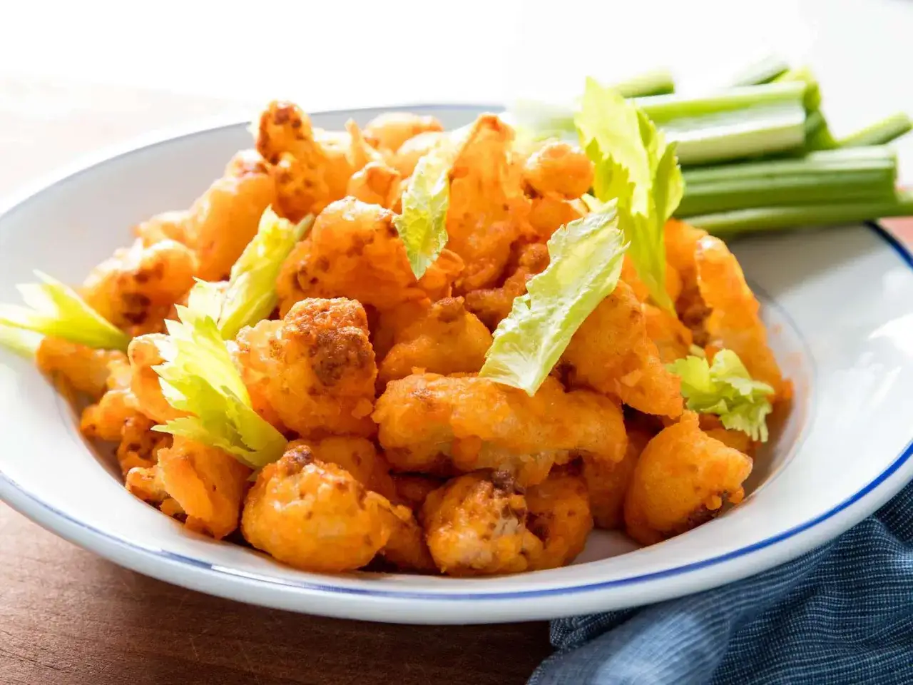 Crujientes alitas de coliflor bañadas en salsa picante, servidas con bastones de apio fresco. ¡Una opción deliciosa y vegetariana!