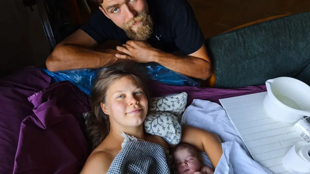 Nybliven mamma med sitt andra barn, en vacker nyfödd bebis. Pappan tittar kärleksfullt på. Kanske känner hon igen gravid andra barnet symtom.