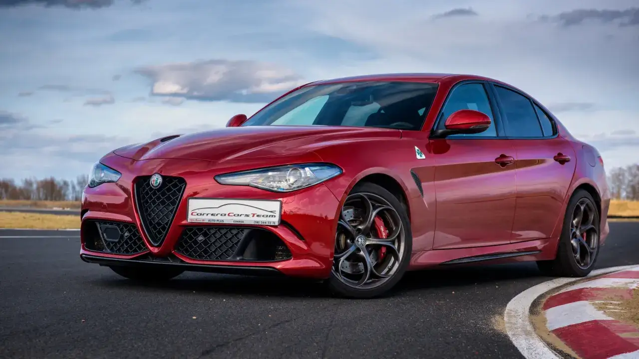 Czerwona Alfa Romeo Giulia Quadrifoglio na torze wyścigowym, z widocznym logo i charakterystycznymi felgami.
