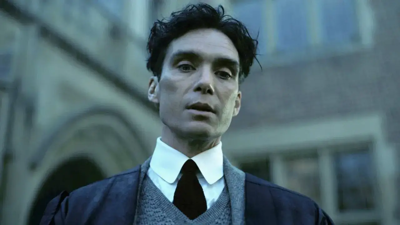 Cillian Murphy w filmach, zamyślony, w eleganckim stroju, na tle budowli.