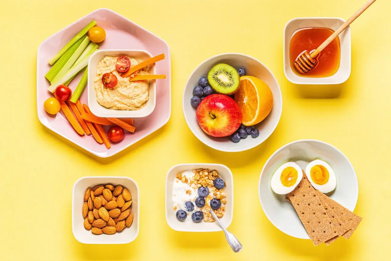 Snacks saludables para nutricionista embarazo: hummus con vegetales, frutas, yogur, almendras, miel y huevo cocido.