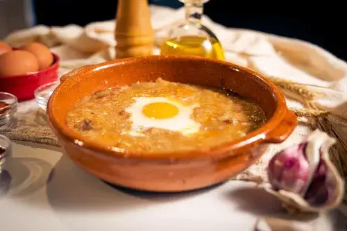 Sopa de ajo con ingredientes separados (ajos, pan duro, pimentón, aceite, caldo, huevo, jamón)