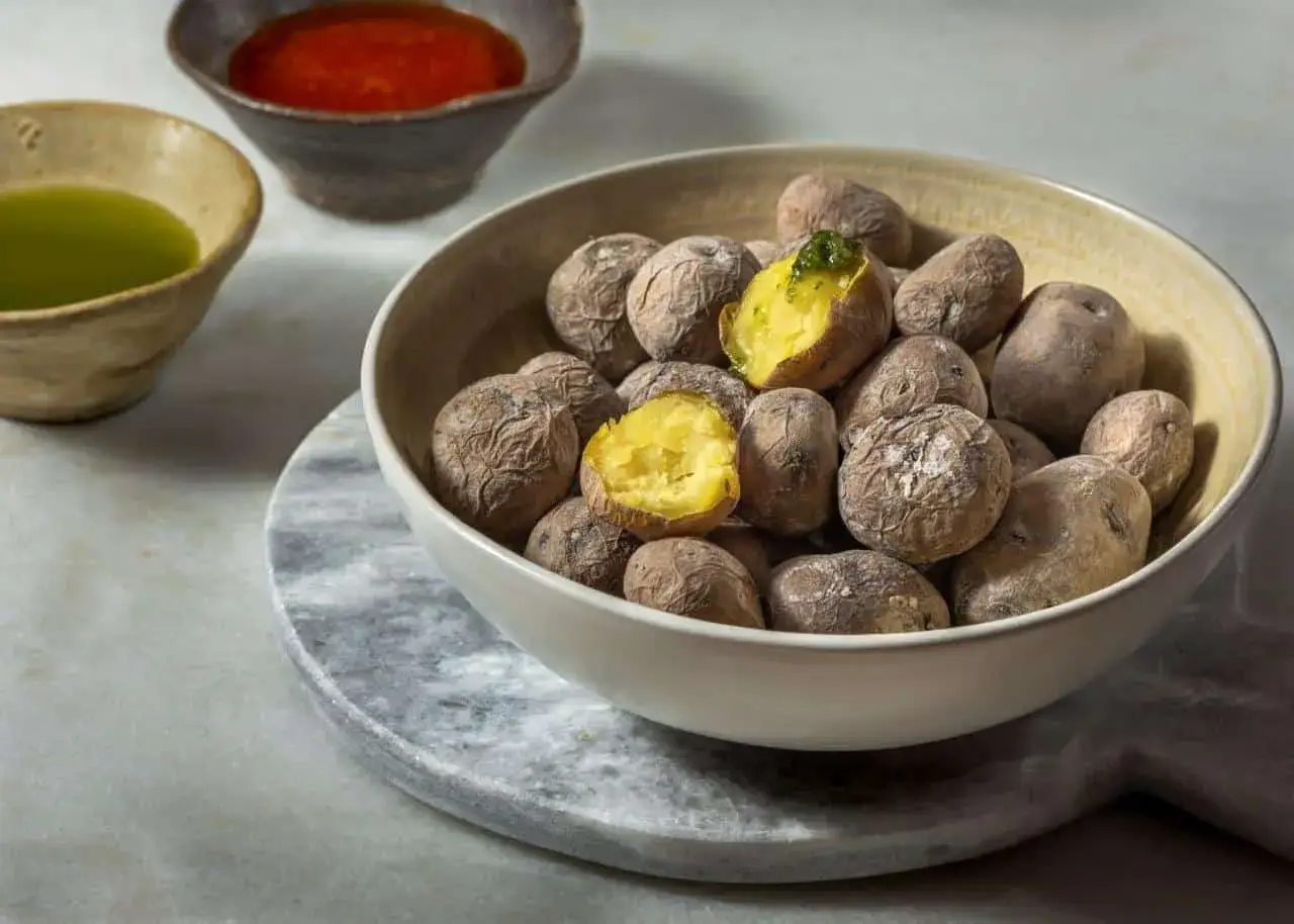 Un tazón lleno de papas arrugadas, algunas partidas por la mitad, con un toque de mojo verde.