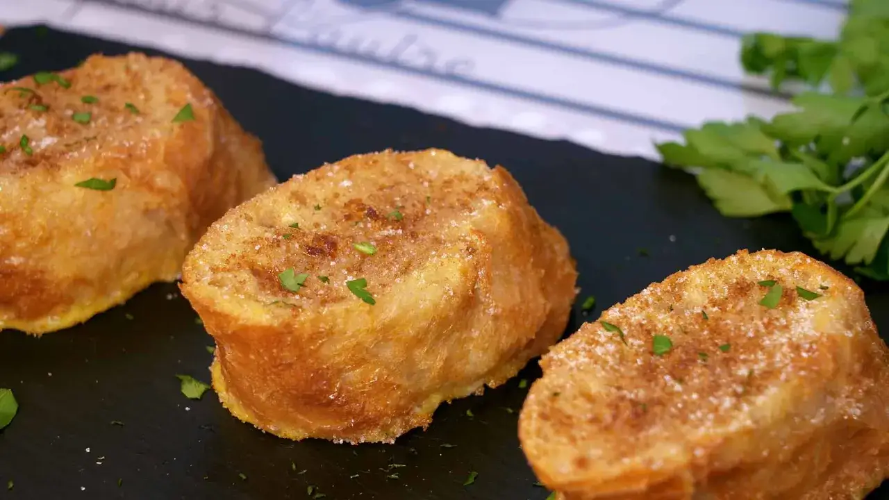 Deliciosas torrijas al horno, doradas y espolvoreadas con azúcar y canela, adornadas con perejil fresco.