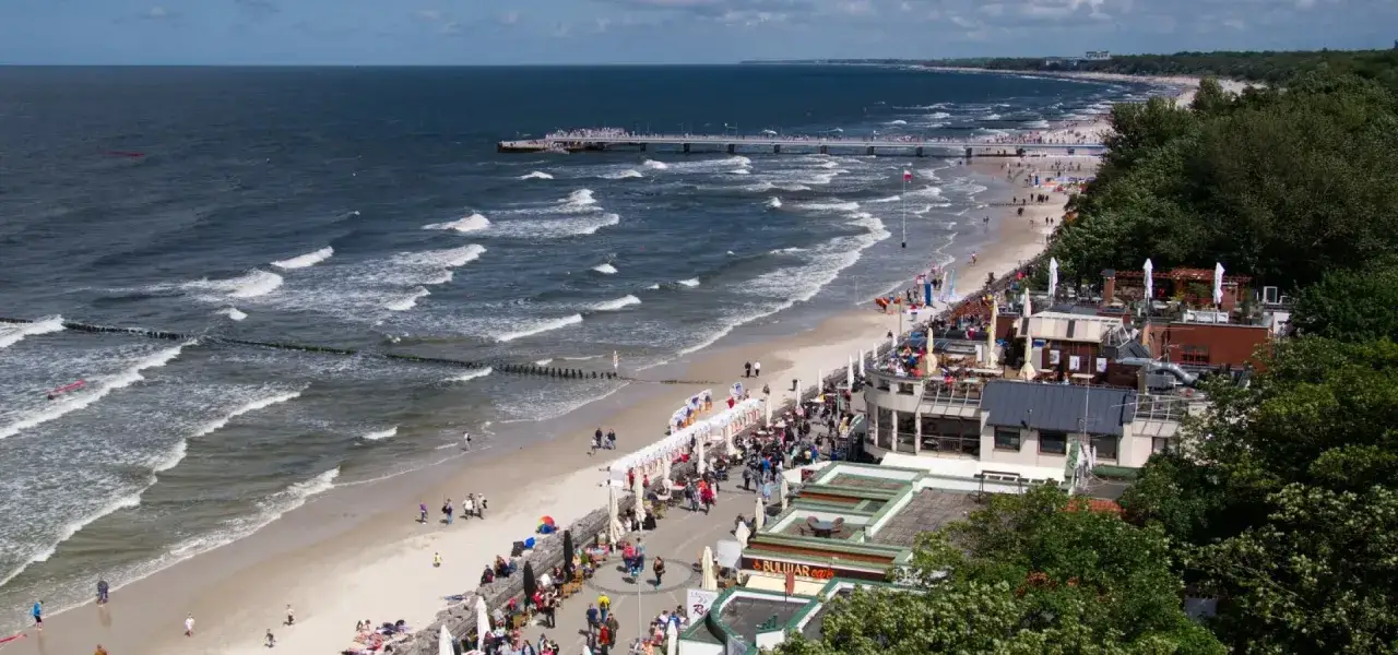 Tętniący życiem deptak Grzybowo atrakcje: plaża, molo, kawiarnie i mnóstwo spacerowiczów cieszących się słońcem i morzem.