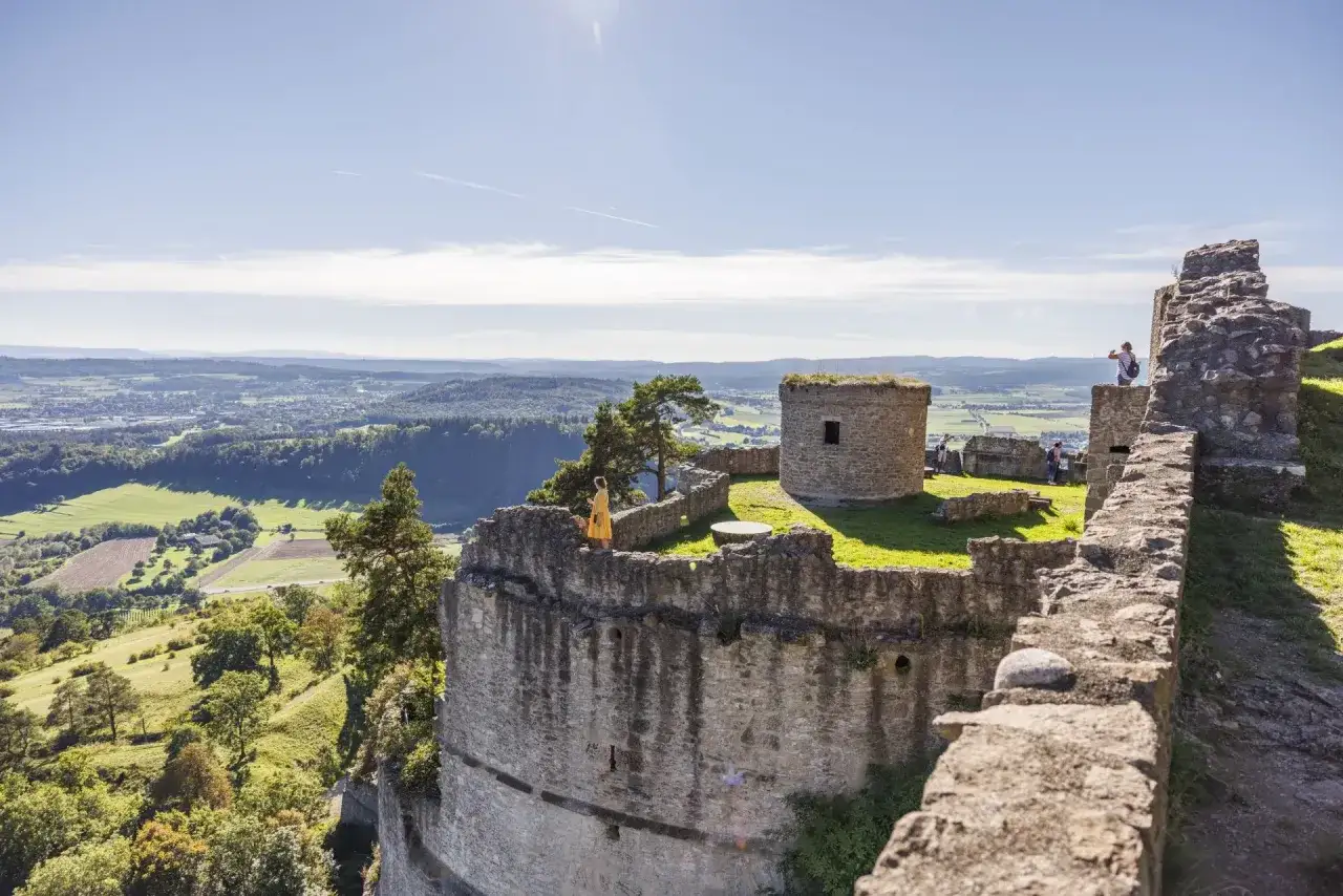 Ruinen der Hohentwiel Burg thronen auf einem Berg. Eine Frau im gelben Kleid genießt die Aussicht über das Tal.