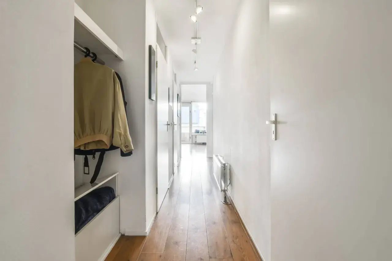 &Eacute;clairage d'un long et &eacute;troit couloir avec des portes blanches, un radiateur et un vestiaire.