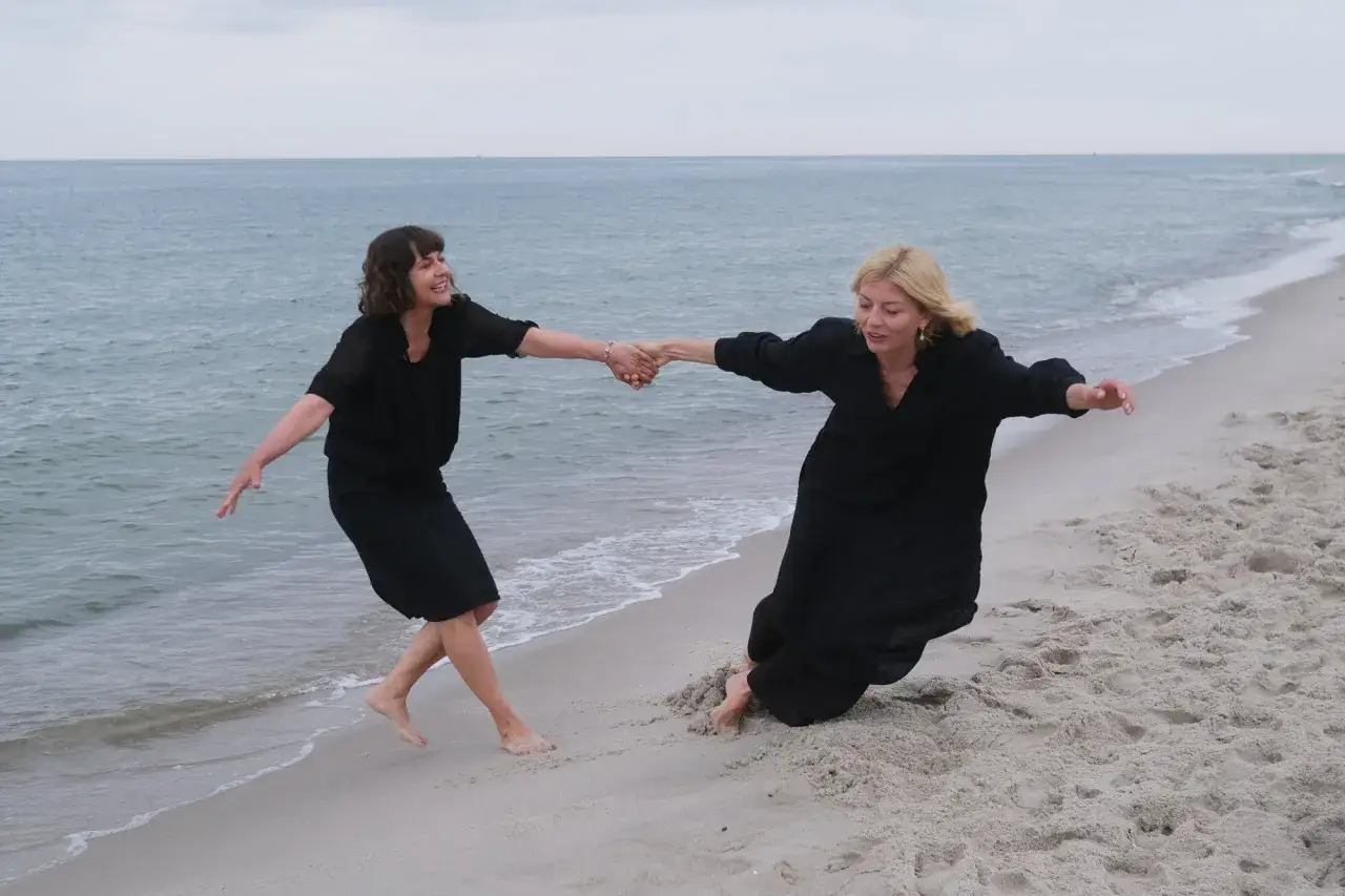 Dwie kobiety w czarnych sukniach tańczą na plaży, trzymając się za ręce. Może to scena z filmu, gdzie kręcono miłość jak miód.